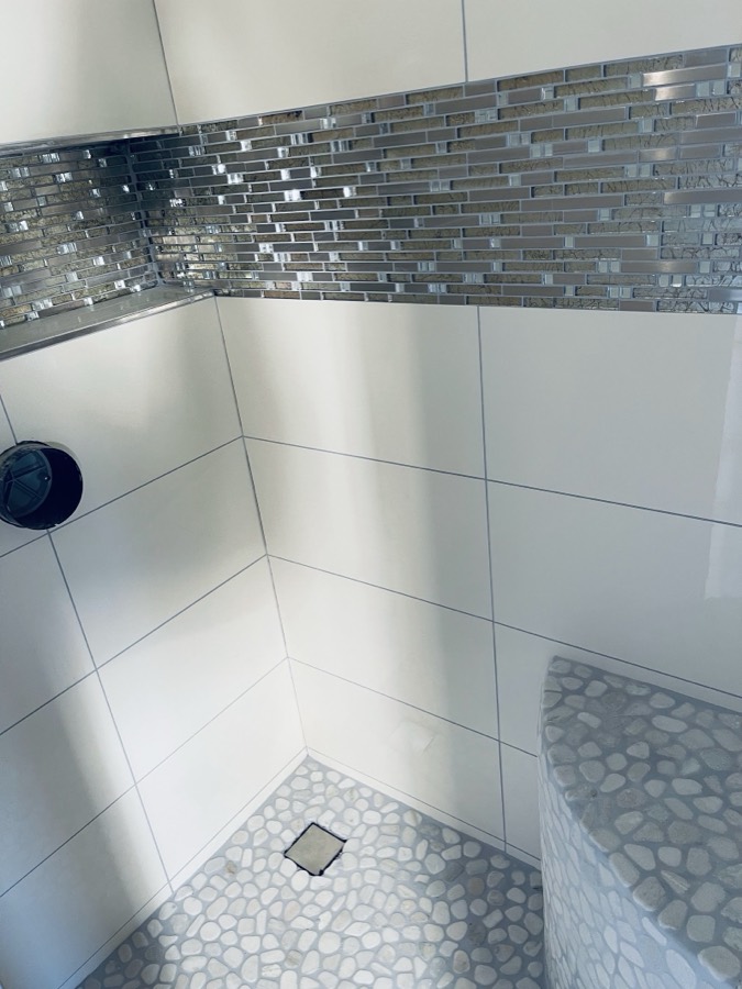 Dusche mit Glasmosaik-Bordüre, weißen Wandfliesen, Kieselboden und gefliester Sitzbank